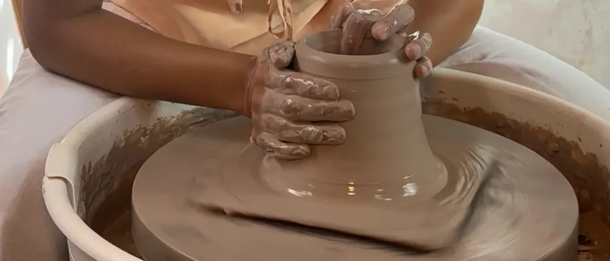 Nancy Lucia at the wheel — both clay-covered hands raising the form